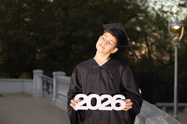 istock Young Graduate Celebrating Accomplishment While Holding 2026 Sign on a Bridge at Sunset 2245421944