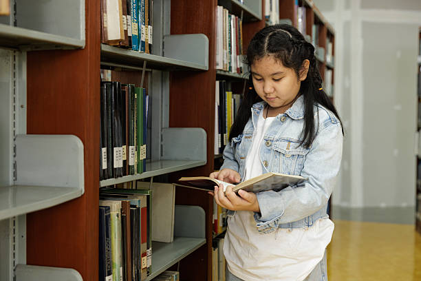 istock Young girl reading book in school library 2245422627