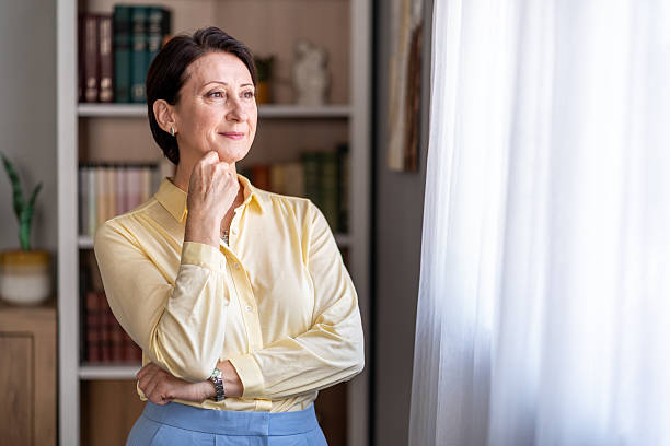 istock Mature woman looking out window dreaming at home 2245422933