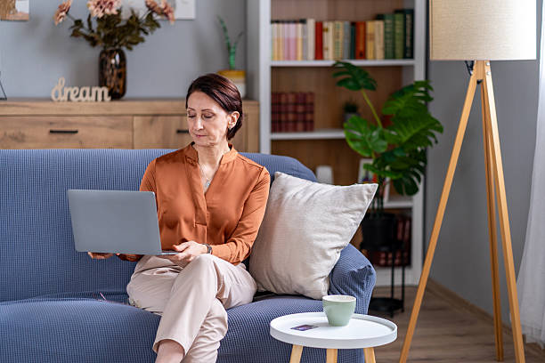 istock Mature woman remotely working on laptop from home couch 2245422973