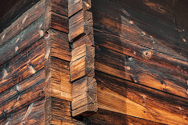 Weathered timber wall with traditional dovetailed corner construction. Showing wood grain, texture, and old material detail