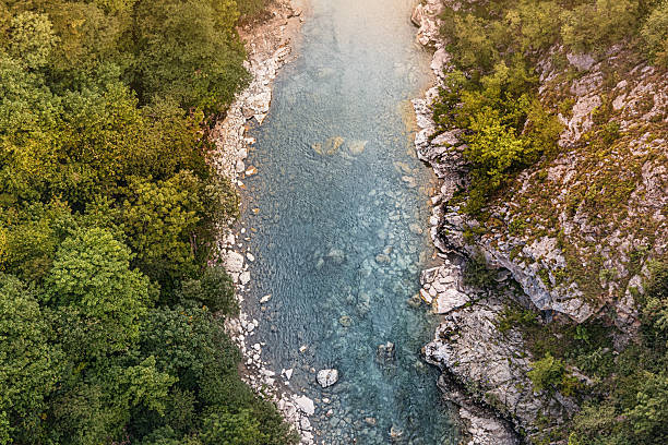 istock River water flowing between green forest and rocky cliffs, showing crystal clear blue water and visible riverbed stones 2245423094