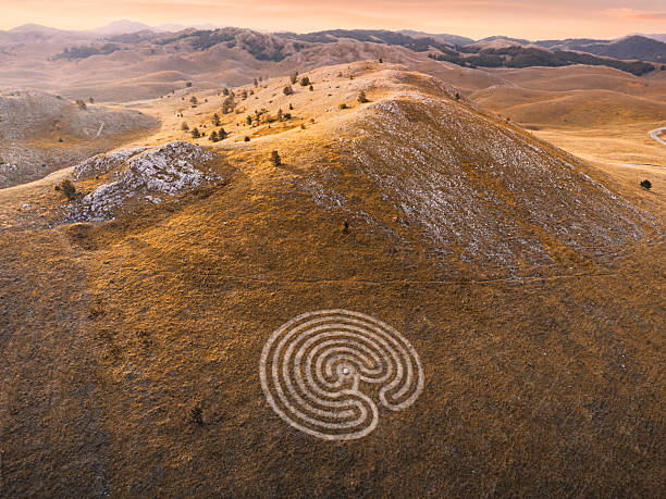 istock Labyrinth carved into a hill on a grass meadow, surrounded by mountains under an expressive sunset sky 2245423117