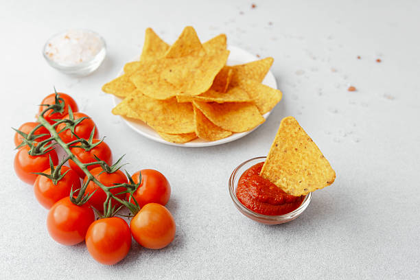 istock Crispy nacho chip in salsa bowl with plate of chips and fresh tomatoes 2245423672