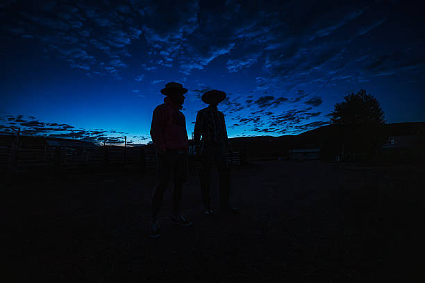 Two ranchers stand outside discussing the day’s plans, silhouetted against a deep blue pre-dawn sky on their family ranch in Western Wyoming.