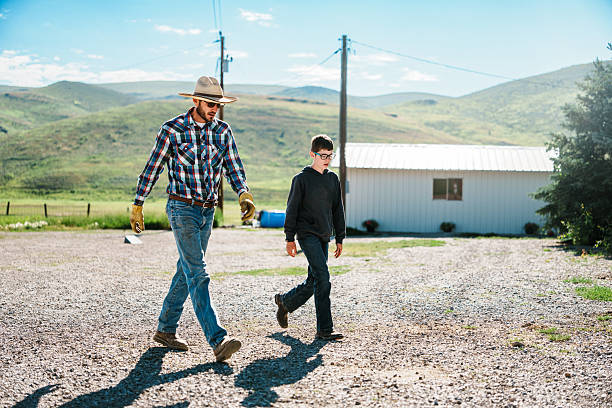 A rancher and his tween son walk and talk along a gravel road on their sunny Wyoming ranch.