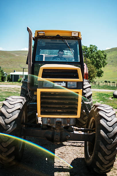 A rancher operates a tractor towing a hay baler, leaving the farmyard and heading to the fields to begin hay harvest on his Wyoming ranch.