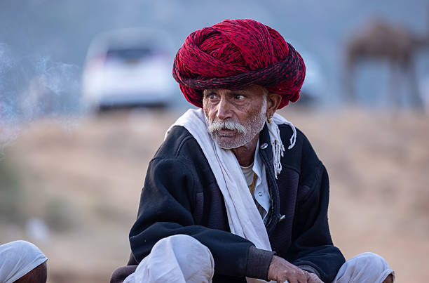 Pushkar, Rajasthan, India - November 2024: Portrait of a rajasthani male in traditional white clothes with colourful turban at desert fair ground during the pushkar camel fair to trade camels.