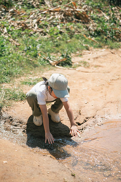 Child Exploring Nature by Stream Water, Touching Water Surface with Hands, Curiosity and Discovery in Natural Environment, Playful Outdoor Experience