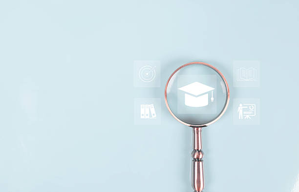 istock Magnifying glass focusing on graduation cap icon on light blue background, symbolizing education research, learning goals, and academic study concept. Ideal for school, university, e-learning design 2245435236