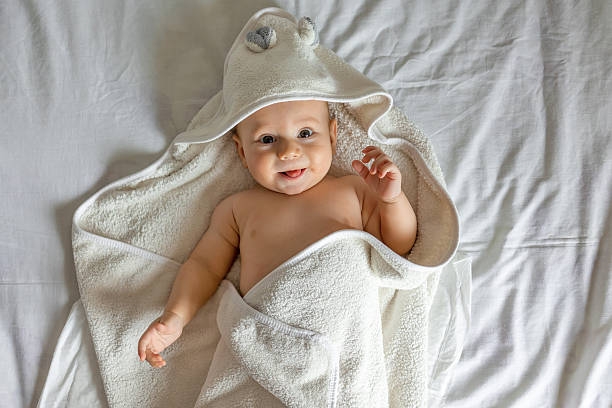 istock Cute happy laughing baby in a soft bathrobe after bathing plays on a white background. The child is wrapped in a clean and dry towel. Washing, baby hygiene, health and skin care 2245441472