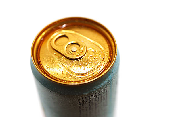 The can shows a shiny golden top with water droplets, indicating that it is cold. The background is bright, emphasizing the refreshing drink.