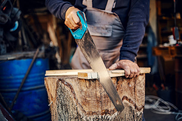 Manual laborer cutting a wooden plank with a handsaw in a rustic workshop. Hands holding the tool during woodworking