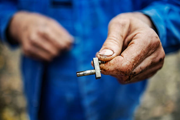 Mechanic's dirty hand holding a small metal car engine part, symbolizing repair, manual labor, and automotive service