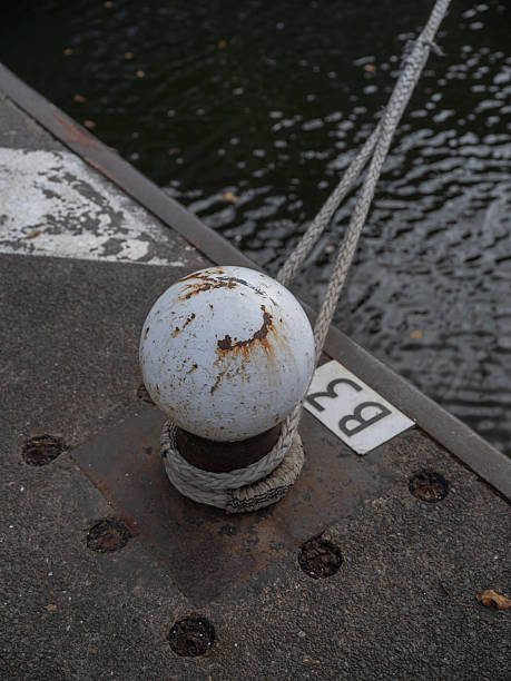 White weathered mooring bollard with rope secured on dock edge with dark water background