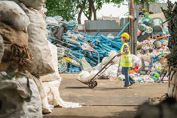 An Asian woman uses a cart to pull and sort trash for recycling.