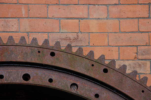 Large metal industrial gear wheel leaning on a brick wall