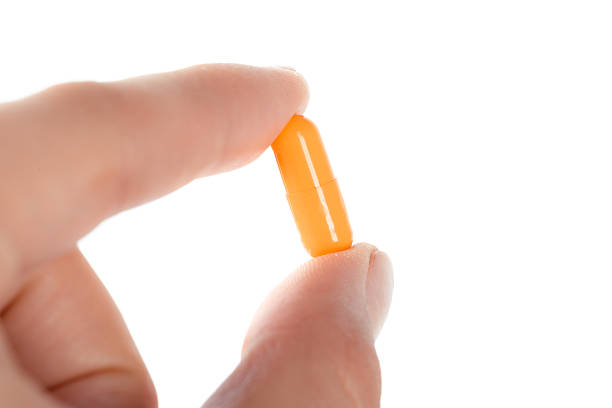 istock Hand holding an orange capsule close to the camera in bright light 2245455019