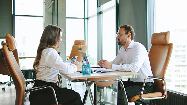 istock A woman and a man are having a focused discussion at a conference table, surrounded by large windows that let in natural light, in a contemporary office setting. 2245458376