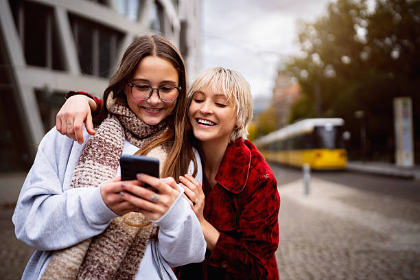 istock Two Young Female Friends Laughing and Hugging While Looking at a Smartphone on a Berlin Cobblestone Street 2245459647