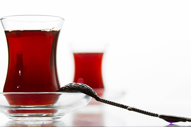 Red tea in clear glasses is accompanied by a silver spoon on a bright table setting.