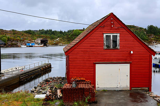 Traditional fishermen's village near Bergen, Norway, featuring rustic red and white wooden houses by the water, a small boat, and rocky coastal landscapes.