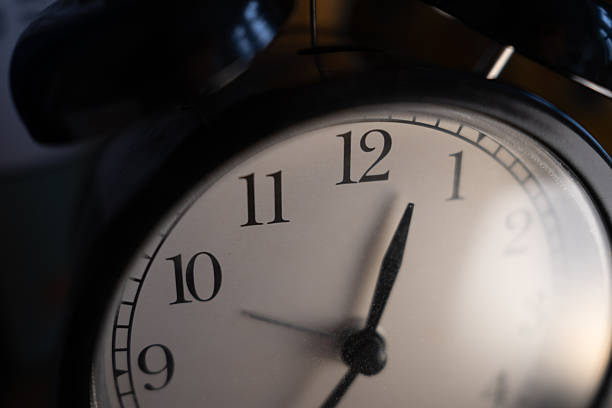 Dramatic close-up of a classic black alarm clock face. The hands near twelve symbolize a deadline, countdown, or new beginning. Moody, focused shot with a shallow depth of field.