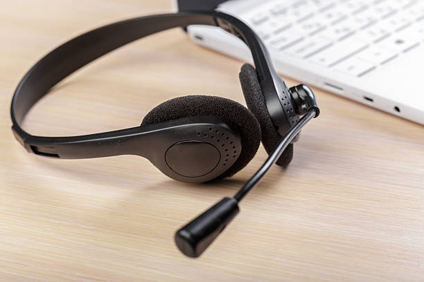 istock Black headset placed on a wooden table next to a laptop with visible keyboard 2245467876