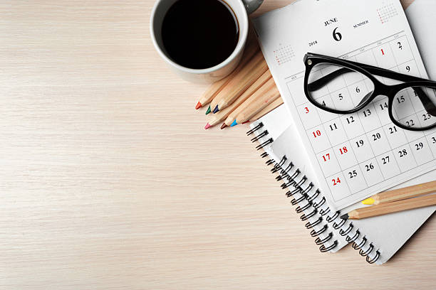 A calendar for June, a notebook, coffee cup, and colored pencils set on a wooden desk.