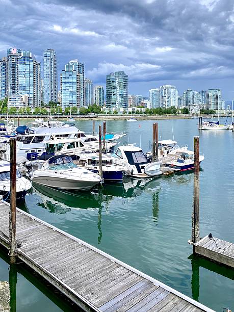Vancouver, Canada – July 14, 2025: Scenic view of a marina with boats and skyscrapers under a cloudy sky in Vancouver, Canada.