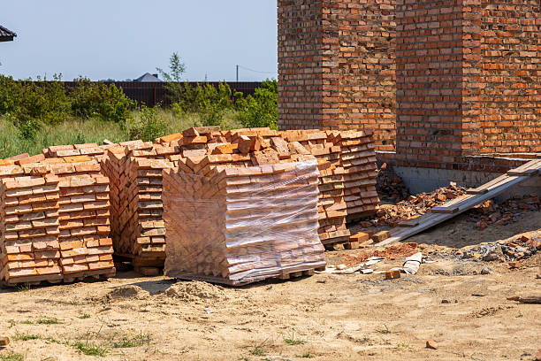 Bricks are neatly stacked on a construction site, prepared for building homes in a growing neighborhood under clear skies.