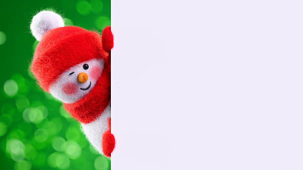 A smiling snowman figurine holds a festive Merry Christmas card with lights twinkling softly in the background, creating a joyful and heartwarming holiday scene indoors.