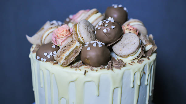 istock Tall white chocolate drip cake is decorated with chocolate truffles, macarons, and flowers 2245473746
