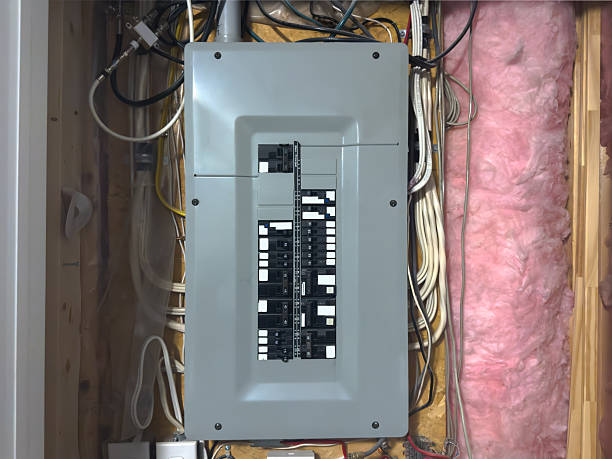 istock Close-up of a residential breaker panel with labeled circuit breakers, exposed wiring, insulation and wooden studs in an unfinished utility area. 2245478039