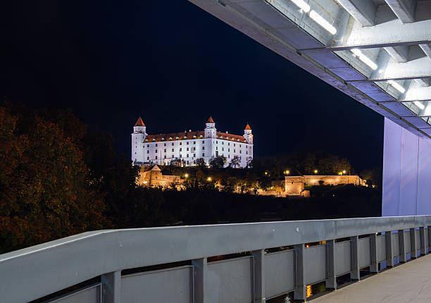 Bratislava, Slovakia - October 18, 2025: Night view of Bratislava Castle illuminated, framed by a modern SNP bridge.