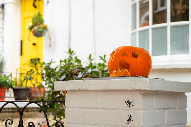 Carved pumpkin (Jack O'Lantern) perched on a wall outside a residential house in the city. The Jack O'Lantern looks as though it is vomiting, as the pulp and seeds of the pumpkin are coming out of its 'mouth'.