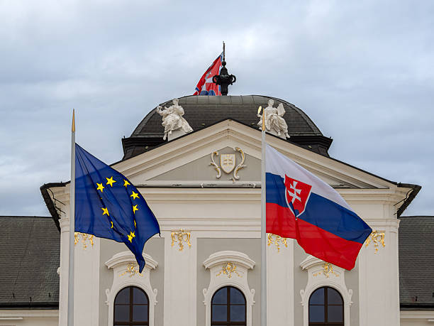 Bratislava, Slovakia - October 20, 2025: Flags of the European Union and Slovakia in front of a presidential palace with sculptures and a cloudy sky.