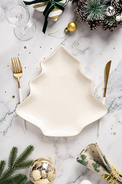 istock A vertical festive Christmas table scene features a unique tree shaped plate, gold cutlery, ornaments, pine branches, and sparkling decor for New Year celebration and holiday greeting 2245480535