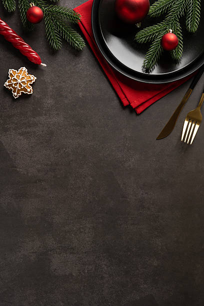 istock Festive vertical Christmas and New Year table scene featuring pine branches, red ornaments, a star cookie, and elegant flatware on a dark background. Ideal for holiday greetings and promotions 2245480538