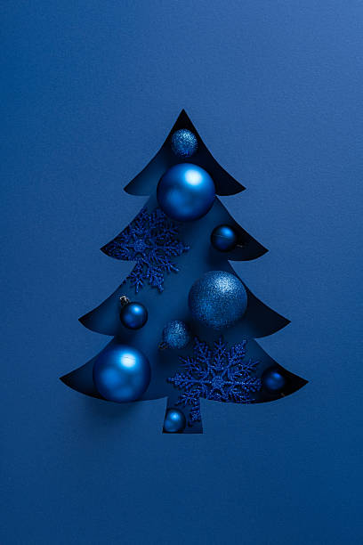 istock A vertical blue Christmas tree cutout decorated with metallic ornaments and snowflakes against a deep blue backdrop 2245480561