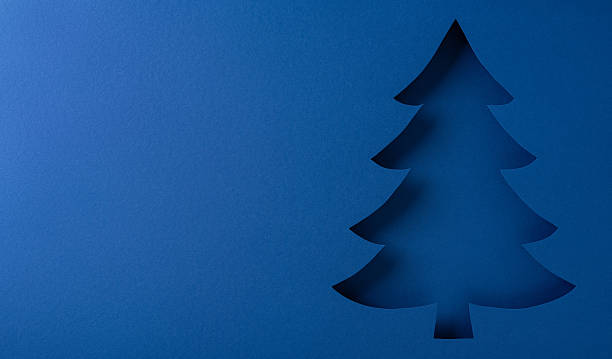 A minimalist blue night scene shows a dark pine tree silhouette, evoking Christmas and New Year warmth. Perfect for festive greeting themes, winter, celebration, and holiday mood in stock projects