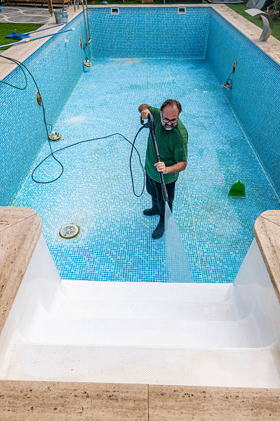 istock Man in flip flops cleaning the swimming pool with a pressurized water 2245480701