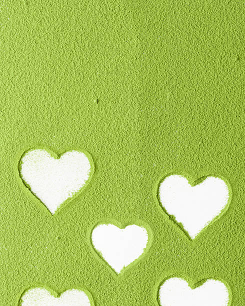 istock Green matcha powder covers white surface with heart-shaped cutouts, creating playful and romantic layout for product or branding design 2245480734