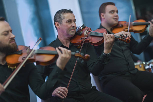 A skilled violinist performs in a live ensemble, concentrating on the bow and strings. The close-up captures the energy and collaboration of musicians in a dynamic orchestral moment.