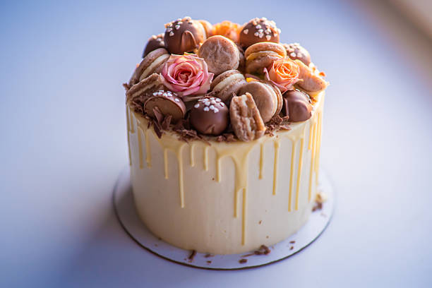 Delicious drip cake decorated with macarons, chocolate and roses standing on white table is perfect for special occasion