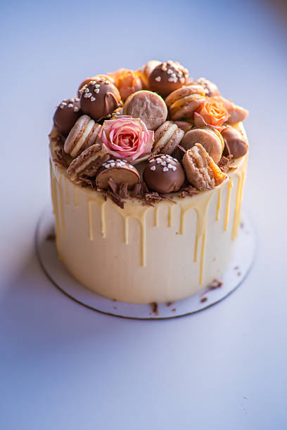 istock Delicious drip cake decorated with macarons, chocolate and flowers standing on white background 2245488680