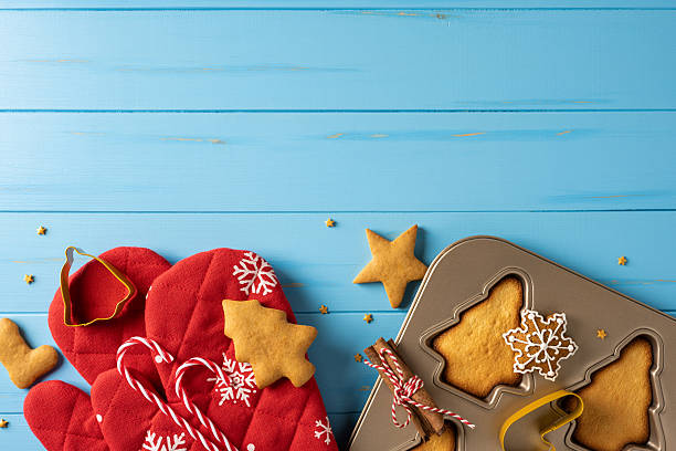 istock Festive holiday baking scene featuring red Christmas mitts, star and snowflake cookies, candy canes, and a baking tray on a blue wooden surface, ready for treats and celebrations 2245492037