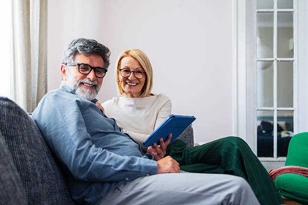 istock Smiling Elderly Couple Relaxing on Sofa With Tablet in Bright Living Room 2245493573