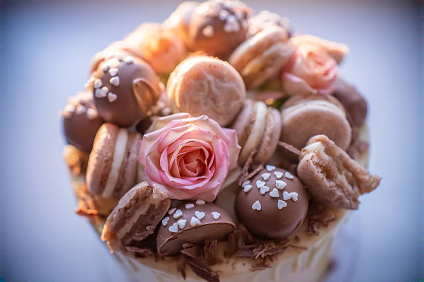 Delicious birthday cake is being decorated with chocolate, macarons, a pink rose and chocolate shavings