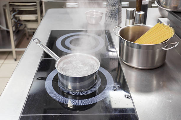 Water simmers in a pot while spaghetti awaits cooking on a stainless steel countertop.